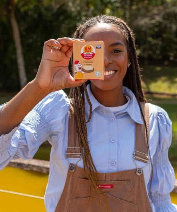 Tofu UAI Tofu com imagem de pessoa sorridente segurando embalagem do produto ao ar livre, em parque natural.