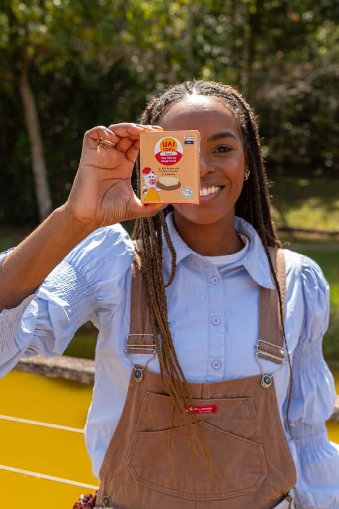 Tofu UAI Tofu com imagem de pessoa sorridente segurando embalagem do produto ao ar livre, em parque natural.